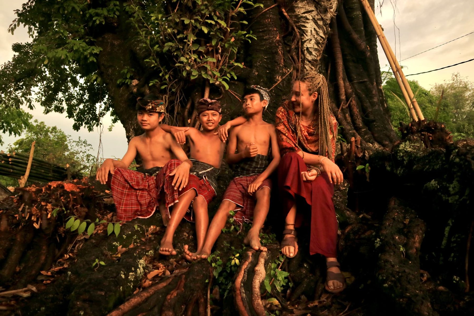 Children from a local community sitting together on the roots of a large tree