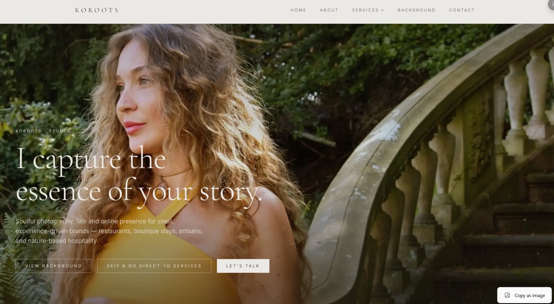 Website of KOROOTS Studio: Marije Andrea in a yellow top against greenery beside a stone staircase